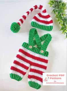 two crocheted christmas stockings and one hat are laying on the table next to a plant