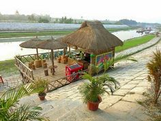 an outdoor restaurant with thatched roof next to a body of water