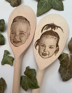 two wooden spoons with faces drawn on them next to green leaves and ivy sprouts