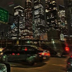 cars are driving down the street in front of tall buildings at night with lights on