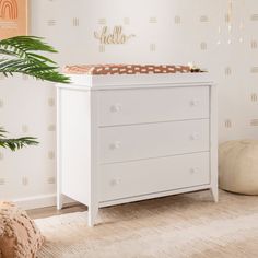 a baby's room with a white dresser and wallpaper