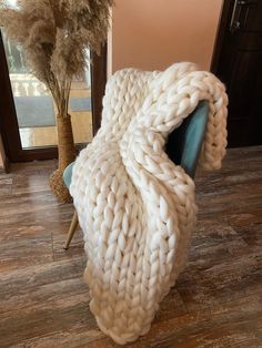 a large chunky blanket sitting on top of a chair next to a plant in a room