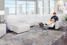 a man sitting on a couch reading a book in a living room with large windows