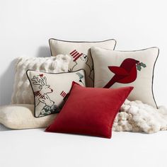 pillows and blankets are arranged on a white surface, with red throw pillows in the foreground