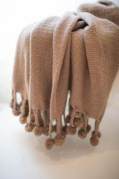 two blankets with pom poms hanging from the ends on a white table top