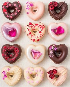 twelve heart shaped donuts arranged in a row on a white surface with pink and red sprinkles