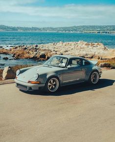 a grey car parked on the side of a road next to the ocean and rocks