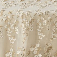 an embroidered tablecloth with white flowers and gold threading on the edge, in front of a beige background