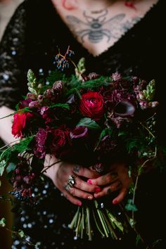 a woman holding a bouquet of flowers in her hands with tattoos on her arm and chest