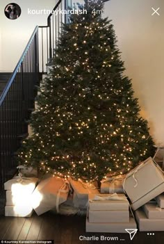 a christmas tree with lots of presents under it and lights on the bottom, next to stairs