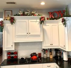 a kitchen with white cabinets and christmas decorations on the top of the cabinet above the stove