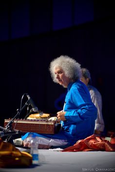 an older woman sitting in front of a microphone and holding a musical instrument on top of a table