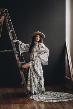 a woman in a dress and hat leaning on a ladder