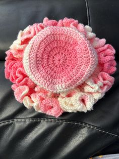 a crocheted pink and white flower on a black leather couch with the center piece made out of yarn