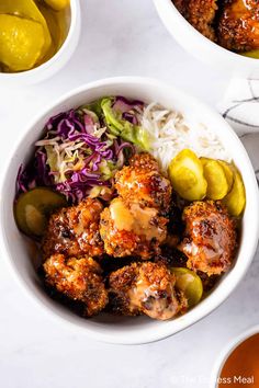 two bowls filled with meatballs, coleslaw and pickles next to lemons