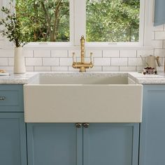 a white kitchen sink sitting under a window next to blue cabinets and counter tops in front of two windows