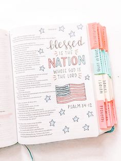 an open bible with the american flag on it and three pens in front of it