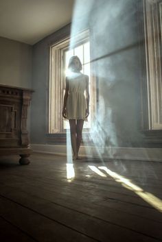 a woman standing in front of a window with the sun shining through her windowsill