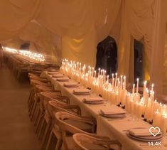 a long table with lots of white candles on it and place settings in front of the tables