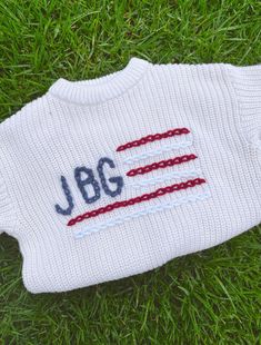 a white sweater with the word jbc on it laying in grass next to a tennis racquet