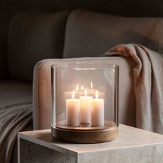 three lit candles sitting in a glass container on a table next to a couch and blanket