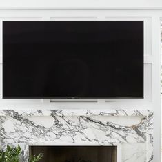 a flat screen tv mounted to the side of a white fireplace with marbled mantle