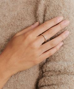 a woman's hand with a gold ring on her left wrist, resting against a beige sweater