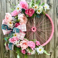 a pink bicycle wheel decorated with flowers and ribbons on a wooden fence, ready to be used as a wreath