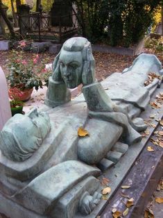 a statue of a woman laying on top of a wooden bench in a cemetery with leaves all over the ground