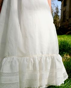 "Antique petticoat with 22\" waist. White cotton with smooth touch and light crispness. Flounce at hem with pin tucks and lace trim. Pale yellow and white ribbon detail at top of flounce. Single button closure at back with \"cheat\" string loop for an additional inch. Flat front waist with tight gathers at back. Very good condition, some small rust spots found on flounce (see last photo for example of majority of it). Measures 34\" long." White Regency Style Petticoat With Ruffles, Daywear Tiered Petticoat With Ruffles, Daywear Tiered Skirt Petticoat With Ruffles, Regency Style Ruffled Petticoat For Daywear, Daywear Ruffled Tiered Skirt Petticoat, Daywear Ruffled Petticoat, White Cotton Petticoat With Attached Cancan, White Ruffled Skirted Petticoat, Vintage Petticoat With Attached Cancan For Summer