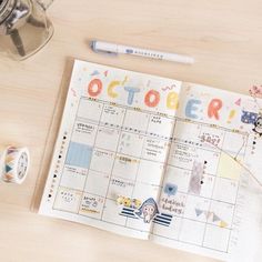 an open planner sitting on top of a wooden table next to a cup and pen