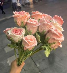 a hand holding a bouquet of pink roses on the street with people walking in the background