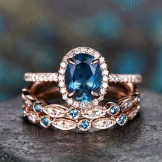 two wedding rings with blue and white stones on top of each other, sitting on a rock