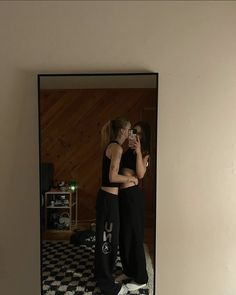 two women standing in front of a mirror with their arms around each other and one woman taking a selfie