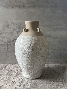 a large white vase sitting on top of a table next to a gray and white wall