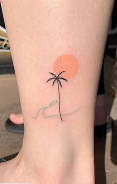 a small palm tree tattoo on the ankle with an orange sun in the back ground