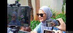 a woman wearing a hijab is taking pictures with her cell phone and camera