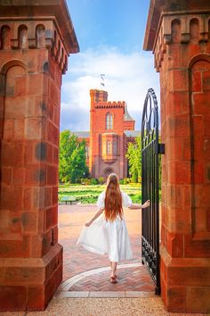 a girl in a white dress is walking through an iron gate into a brick building