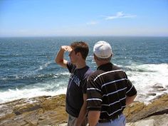 two men looking out at the ocean from a cliff