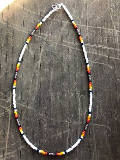 White, light blue, black, red, orange, and yellow beaded necklace. Multicolor Southwestern Style Beaded Chain Jewelry, Multicolor Southwestern Beaded Chain Jewelry, Southwestern Style Multicolor Jewelry With Black Beads, Southwestern Multicolor Beaded Chain Jewelry, Southwestern Style Multicolor Beaded Chain Jewelry, Southwestern Multicolor Beaded Jewelry, Southwestern Style Colorful Beaded Choker Necklace, Adjustable Orange Necklaces With Black Beads, Adjustable Orange Necklace With Black Beads