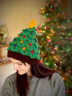 a woman wearing a knitted christmas tree hat in front of a decorated christmas tree