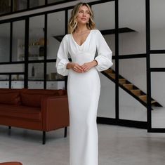 a woman in a white dress standing next to a couch