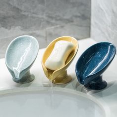 three different colored soaps sitting on top of a white sink next to a faucet