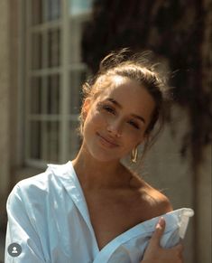 a woman in a white shirt posing for the camera with her hand on her chest