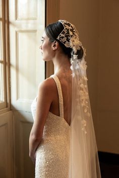 a woman in a wedding dress looking out the window with her veil draped over her head