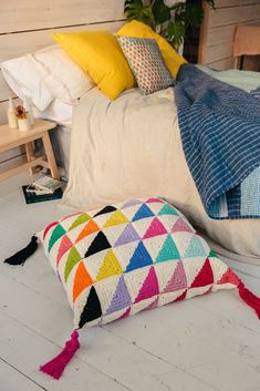 a multicolored pillow sitting on the floor next to a bed with white sheets and pillows