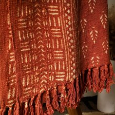 an orange and white blanket sitting on top of a wooden table next to a vase