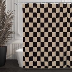 a black and white checkered shower curtain next to a toilet in a bathroom with a potted plant