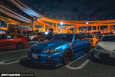 there are many cars parked in the parking lot at night time, and one is blue