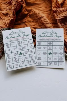 two wedding seating cards sitting on top of a table next to an orange cloth covered bed